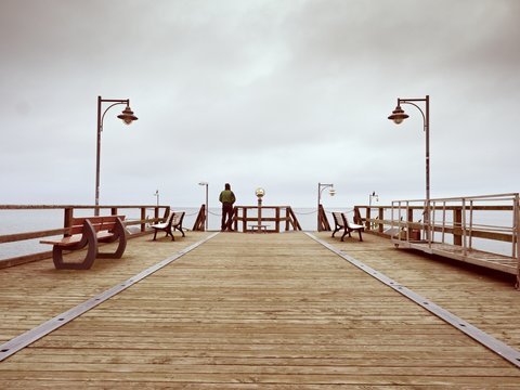 Adult Tall Man On Pier Board Look Over Sea To Morning Fall Horizon. Smooth Water Level