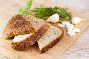 Куски ржаного домашнего  хлеба, чеснок и зелень на разделочной доске