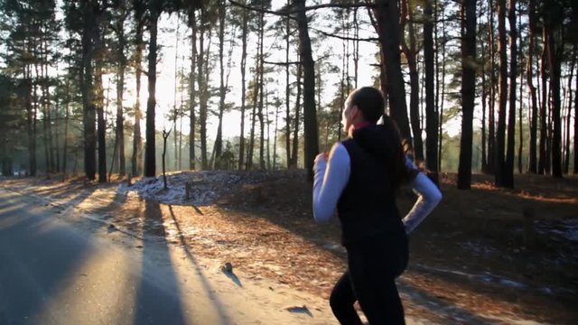 Young woman with a slender figure is engaged in gymnastics at sunrise. She makes a run along the forest. Camera stabilizer steadycam shot.