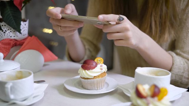 Woman's hand photographing her coffee sitting at the cafe for social network, On the table in the coffee shops were doing cappuccino cupcakes. Women's hands holding smart phone