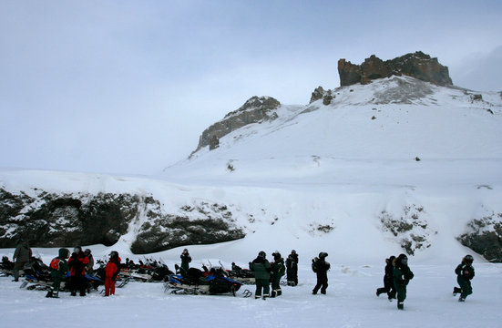 The group of tourists with snowmobiles stop near the mountain.