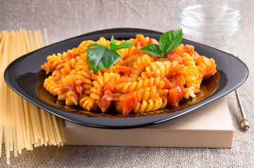 Pasta girandole on a black plate with vegetable sauce