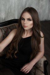 Young girl with long beautiful hair and smoky eyes wearing black maxi evening dress. Studio shot