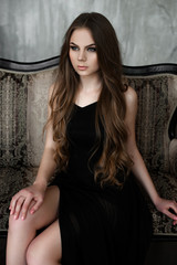 Fototapeta na wymiar Young girl with long beautiful hair and smoky eyes wearing black maxi evening dress. Studio shot