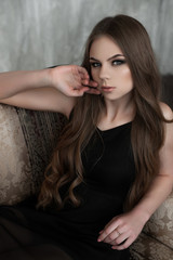 Naklejka premium Young girl with long beautiful hair and smoky eyes wearing black maxi evening dress. Studio shot