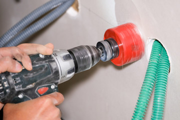 electrician holding power drill with gypsum hole saw making hole in plasterboard