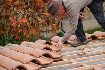 construction worker on a renovation roof covering it with tiles