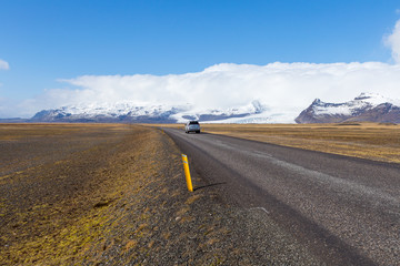 Car touring the ring road passes a tongue of the Vatna Glacier in Iceland with mountain peaks covered in clouds
