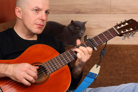 the man sitting on the sofa with the cat plays classical guitar