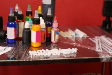 Bottles with inks and needles for tattoo machine on wooden table, close up view