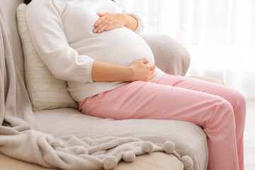 Closeup of pregnant woman touching belly and sitting on sofa at home