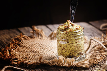 Mustard sauce in a glass jar with a spoon, wooden table, selecti