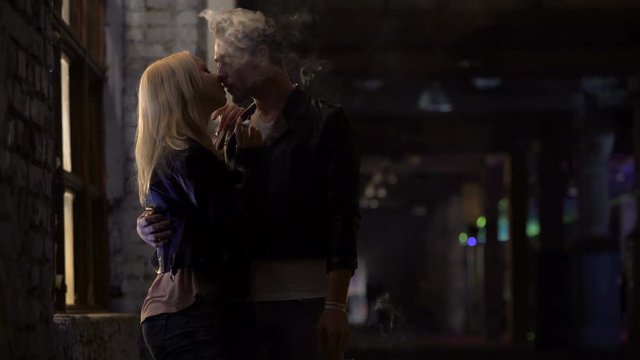 Drunk couple smoking and kissing passionately at night club, bad habits
