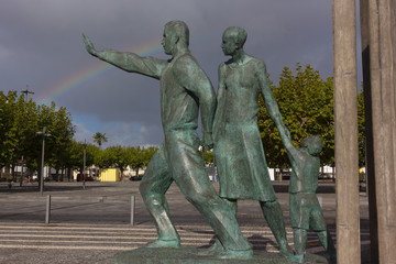 A statue commemorating migrants in Ponta Delgada, Azores, Portugal. The monument and rainbow across...