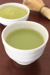 Matcha green tea on wooden table in soft-focus in the background. over light