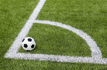 The soccer football in the corner on the artificial green grass field