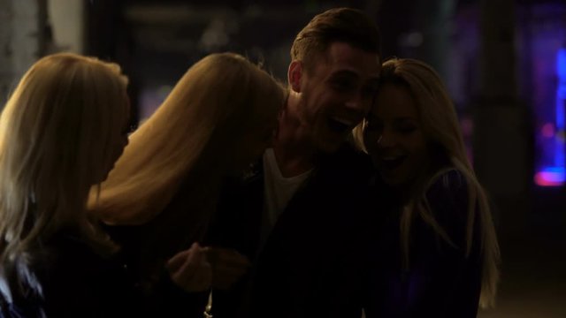 Three beautiful blond women flirting with man at night club, relaxation, hook-up