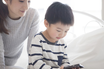 Obraz premium Mother and child are watching smartphone together in the bedroom