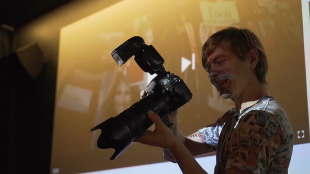 Young professional photographer with big camera works. On it shines on the projector. Slow motion.