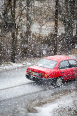 Obraz na płótnie Canvas A red car is driving in a snow blizzard. The car is out of focus. Dangerous weather to drive. Heavy snowfall on a winter day.