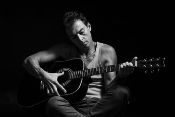 Black and white, low key portrait of caucasian man that play his acoustic guitar