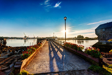 Sun rises over the Piscataqua River and the Portsmouth Navy Yard as seen from Prescott Park, Portsmouth, NH - obrazy, fototapety, plakaty