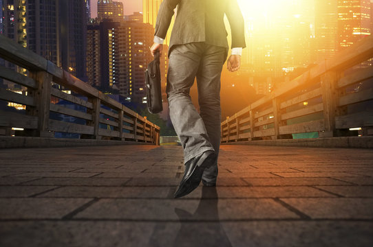 Young manager carrying a briefcase while walking on the road / bridge toward a city