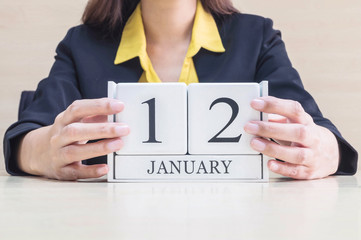 Closeup white wooden calendar with black 12 january word in blurred working woman hand on wood desk in office room , selective focus at the calendar
