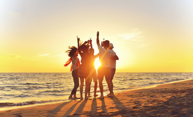 group of happy young people dancing at the beach on beautiful summer sunset