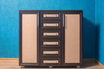 The brown dresser with beige inserts is photographed in an interior against the background of a blue wall