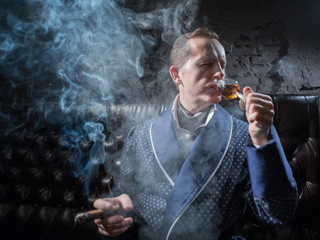Fototapeta premium Man in his office smoking a cigar and drinking brandy