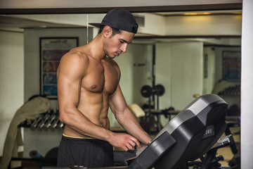 Shirtless young man running on treadmill in gym