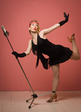Pretty actress in black retro dress singing with microphone