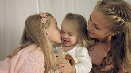 Mother kissing little daughters and their toy