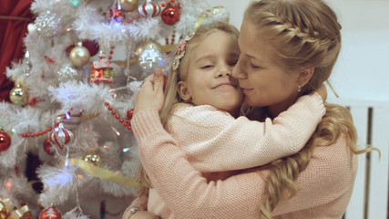 Mother and daughter hug and kiss each other near a Christmas tree