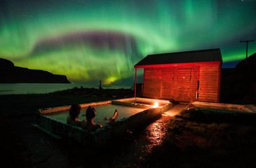 Relaxing in geothermal hot pool under northen lights (Aurora Borealis) in Iceland