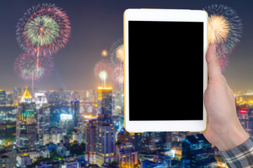 Male hand holding a tablet touch computer gadget with touch blank screen on blurred city landscape and firework background.