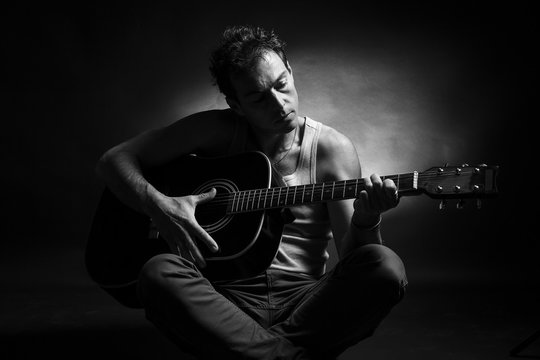 Young caucasian man play a acoustic guitar. Black and white picture, low key studio portrait