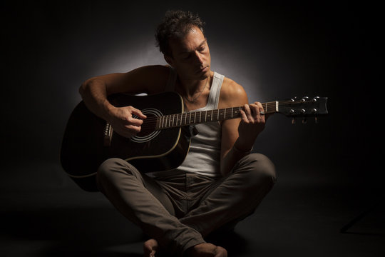 Young caucasian man play a acoustic guitar. Low key studio portrait