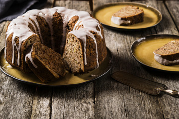 Banana cake with apples and walnuts drizzled frosting and sliced pieces on plates with effect craquelure on the shabby wooden background. Selective focus 