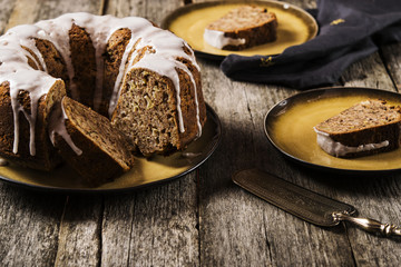 Banana cake with apples and walnuts drizzled frosting and sliced pieces on plates with effect craquelure on the shabby wooden background. Selective focus 
