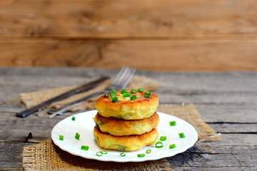 Vegetable patties on a plate, fork, knife on wooden table. Fried patties cooked of potatoes, green peas, carrot and green beans and garnished with fresh green onion. Delicious vegetable meal