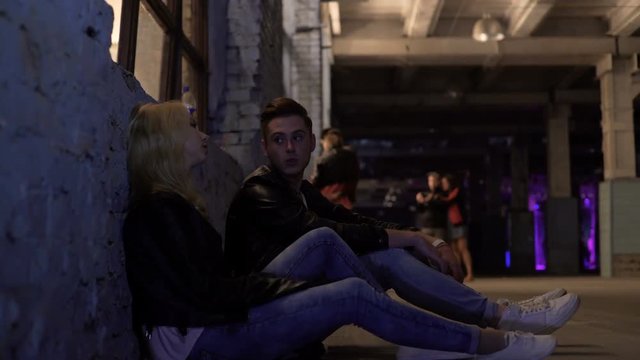 Blonde woman and man sitting near wall and talking, after-party, night life