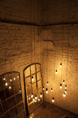 The light source in the interior. Designer light bulbs in the interior with a mirrored window on the brick wall background. Lamps hanging from the ceiling.