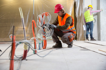 Fototapeta premium Portrait of a worker, constructing and checking development of a small business hall. Reliable civil engineer working on a construction site, foreman at work, another man in the background