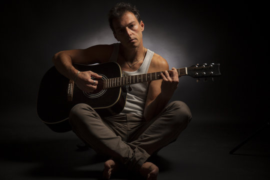 Young caucasian man play his acoustic guitar in a dark room