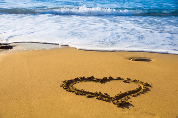 Drawing a heart on the beach sand on the beach with sea waves in the background. Selective focus. Beautiful deserted beach.