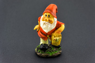 Dwarf figurine with red hat and holding a bucket in the hand isolated on black background.