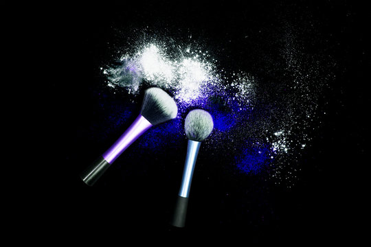 Makeup brushes with powder spilled glitter dust on black background. Blue powder on black table.