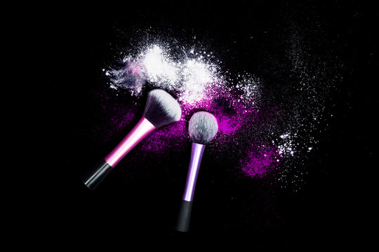 Makeup brushes with powder spilled glitter dust on black background. Purple powder on black table.